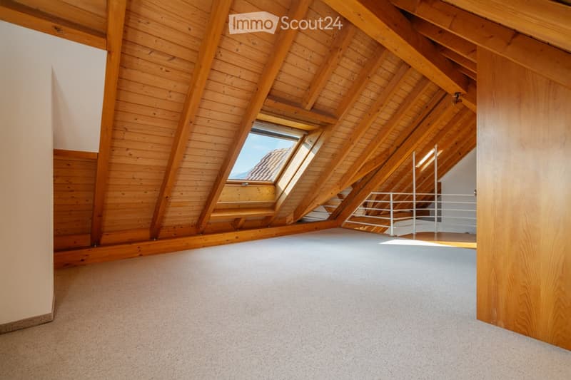Empty attic room with wooden beams, skylight windows, and a metal railing leading to another area.
