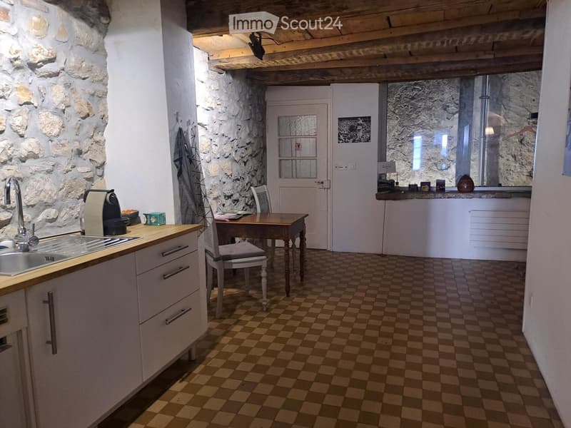 Cozy kitchen with stone walls, checkered floor, white cabinets, sink, coffee maker, and a small table with a chair.
