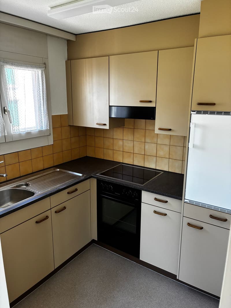 Modern kitchen with light-colored cabinets, stainless steel sink, electric stove, and built-in oven. Beige tiles and grey countertops.