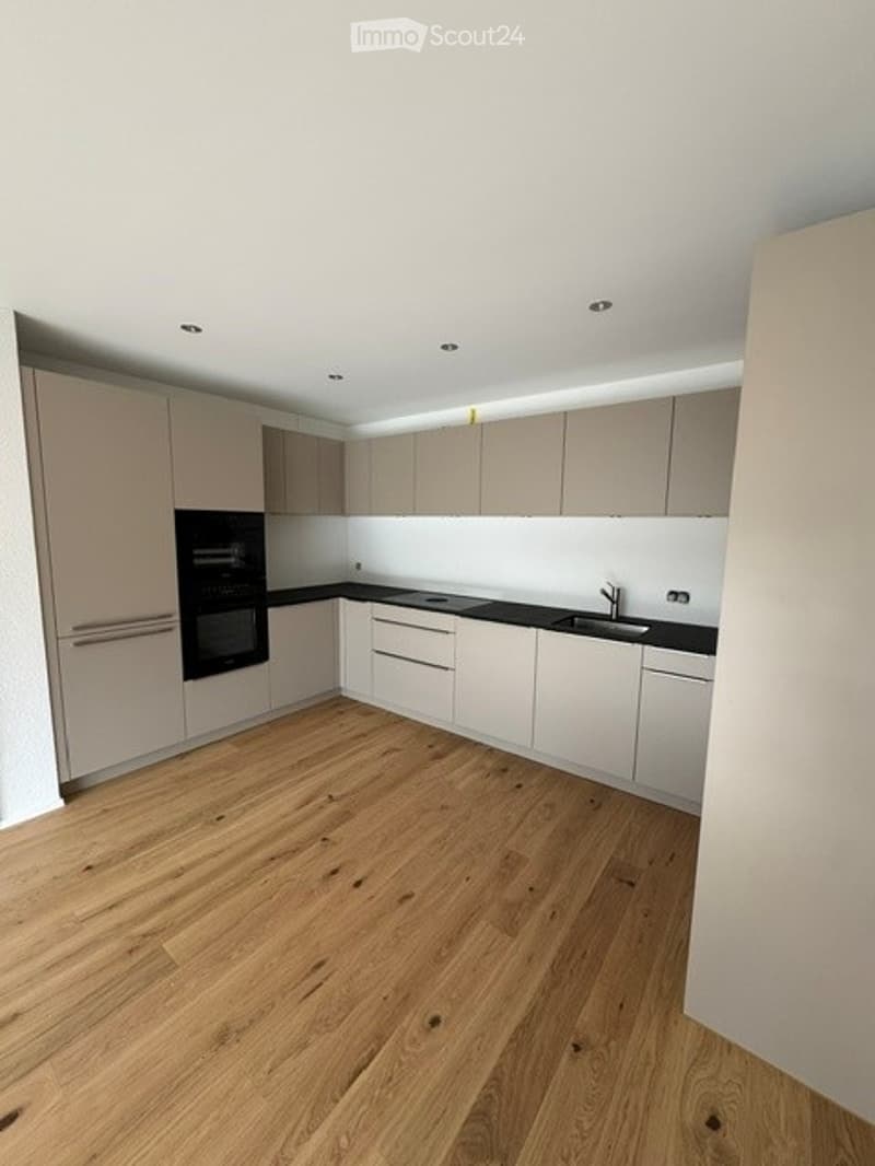 Modern kitchen with light-colored cabinets, a black countertop, and a wooden floor. Features an oven, sink, and faucet.