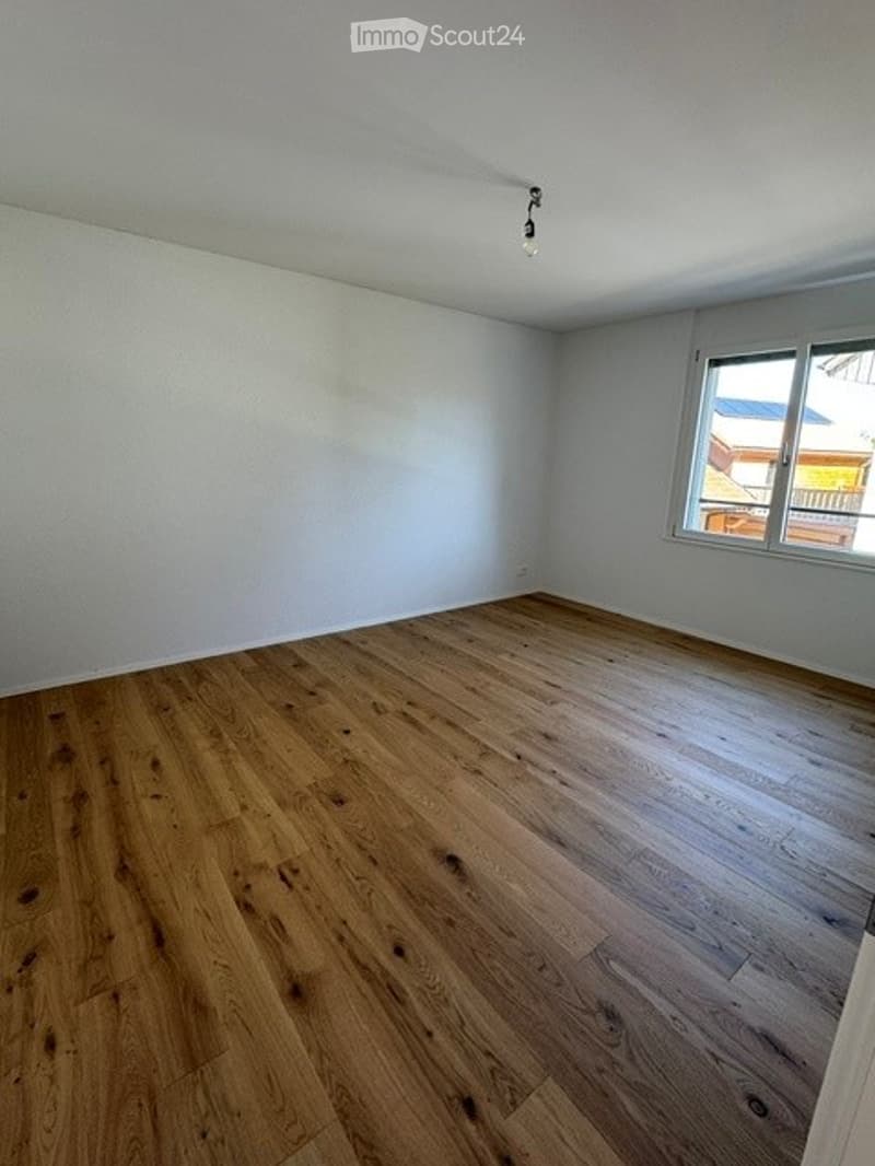 Completely empty room with light wooden flooring and white walls. A single window with white frame is visible on one wall.