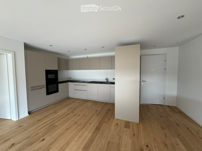 Modern kitchen with light-colored cabinets, a central island, and wooden flooring. Features include a sink with a faucet and an oven.