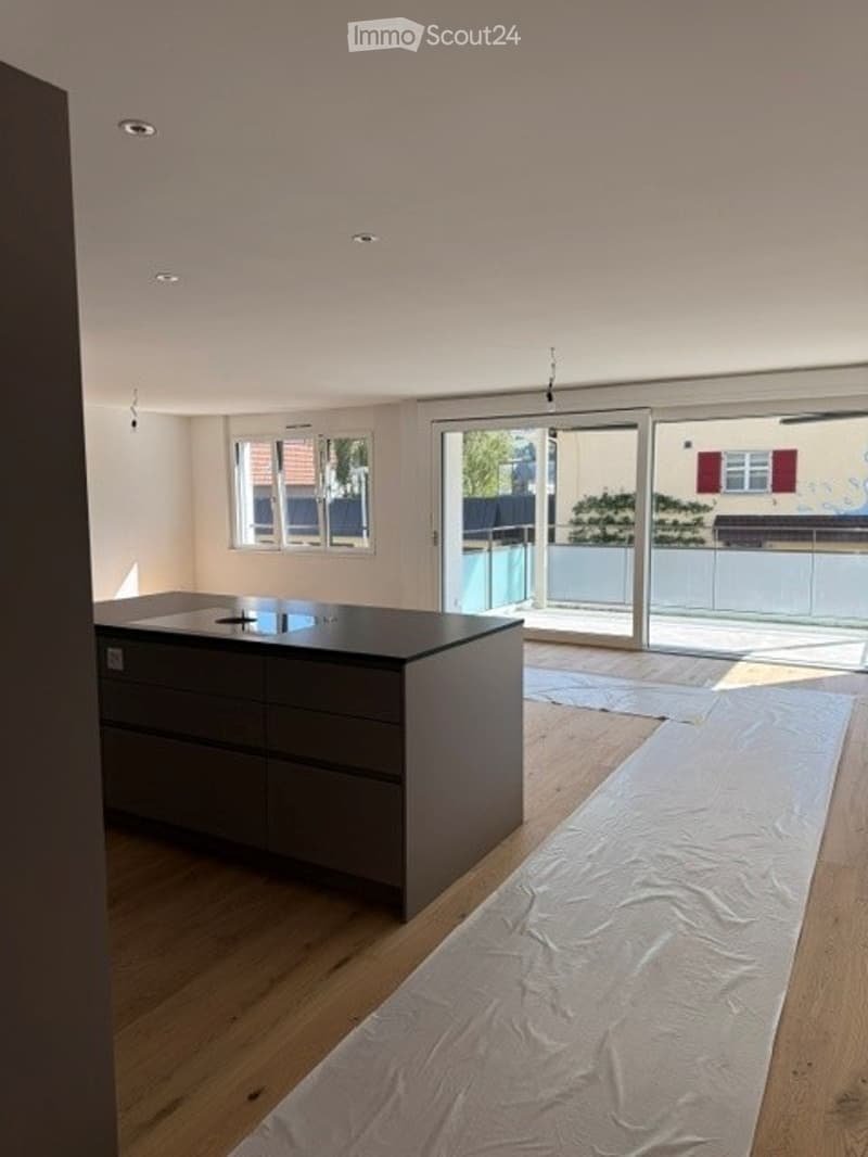Empty kitchen with wooden flooring, dark grey cabinetry, and large sliding glass doors leading to a balcony.