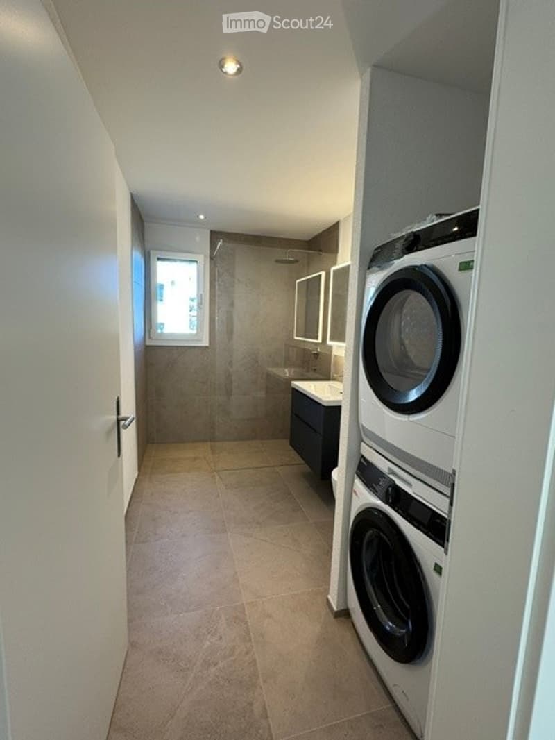 Modern bathroom with a tiled floor, a sink with a mirror, a shower area, and a stacked washer/dryer unit.