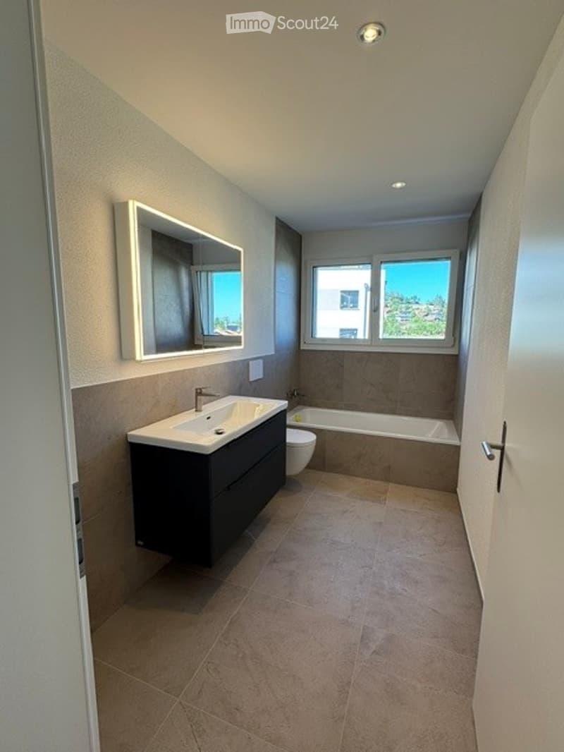 Modern bathroom with a large mirror, sink, bathtub, and toilet. Natural light from windows offers a scenic view.