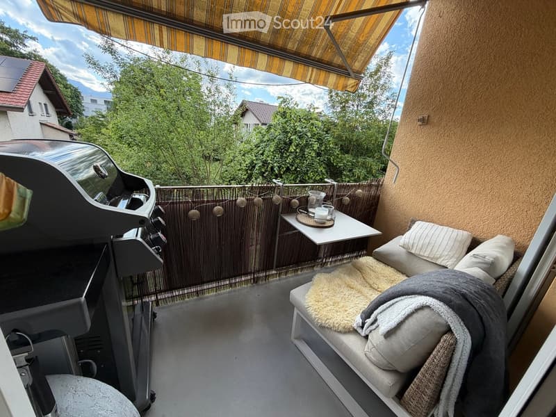 Balcony with a sofa, a small table with cups, a grill, and a decorative string of lights.