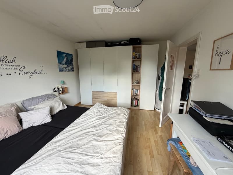 Cozy bedroom with a single bed, white wardrobe, bookshelf, small table with laptop, and decorative wall art.