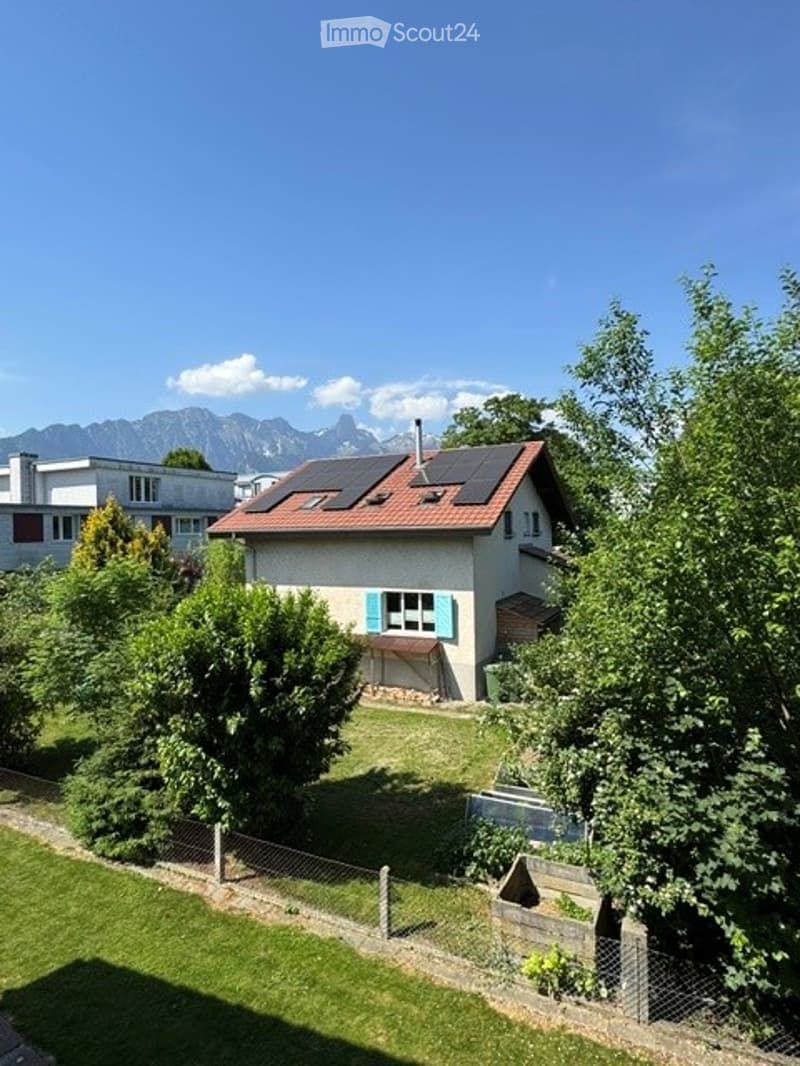 Single-family house with red-tiled roof, solar panels, white walls, and blue shutters. Surrounded by greenery and a well-maintained lawn.