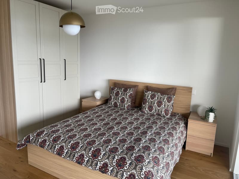 Wooden bed with paisley bedding, two nightstands, a wooden cabinet, a large white wardrobe, a pendant light, and wooden flooring.