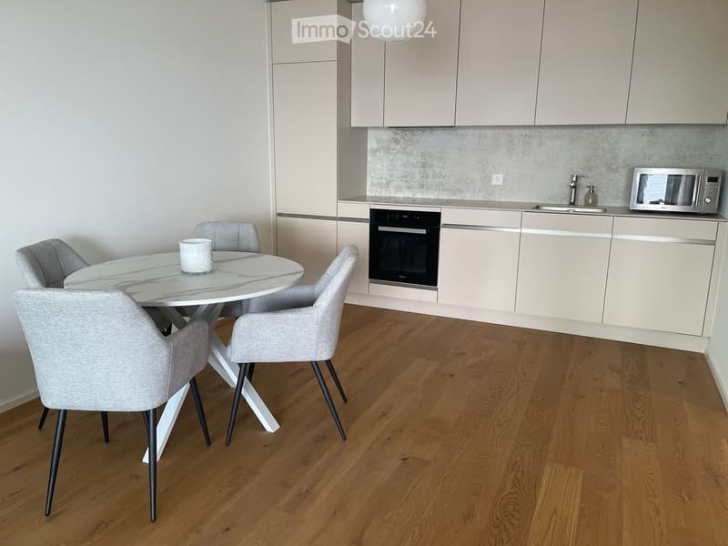 a modern kitchen with a dining table, wooden floor, and neutral color scheme, featuring a microwave, a sink, and built-in oven