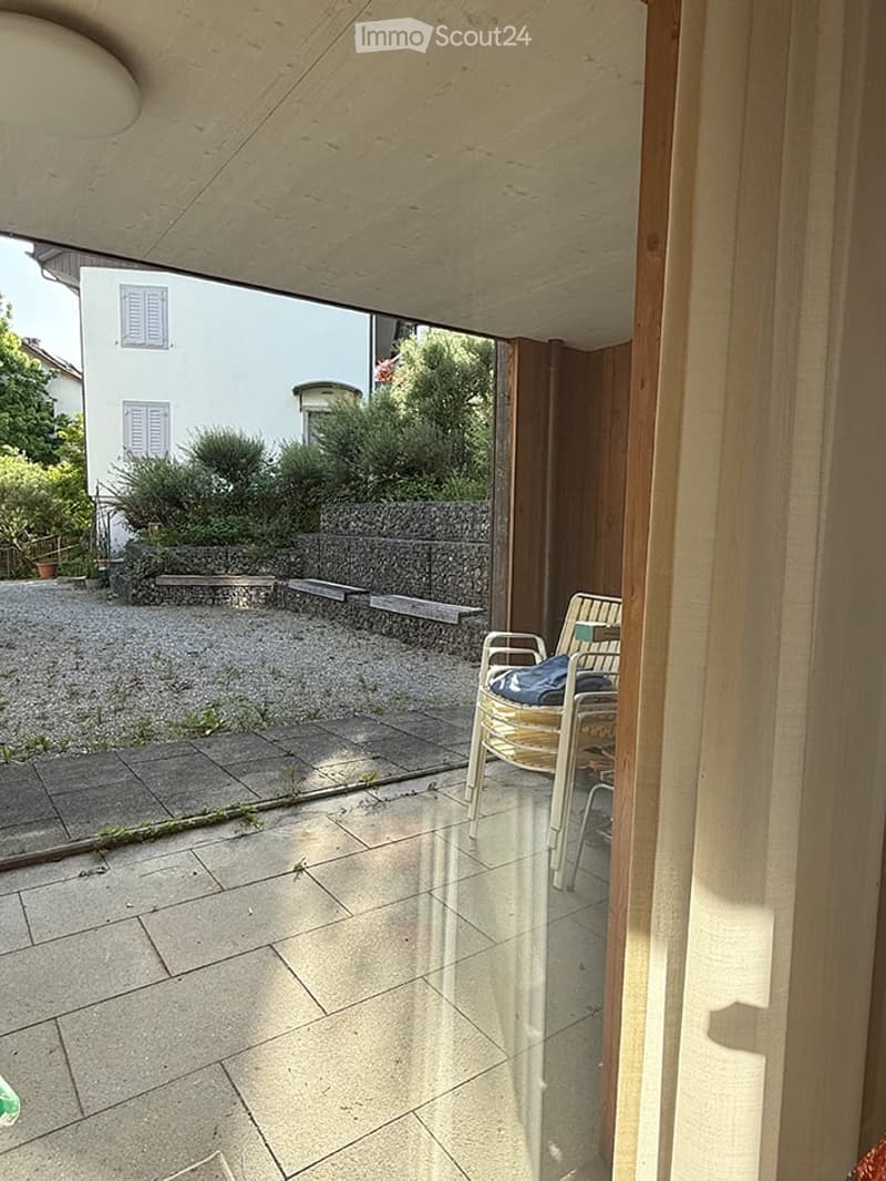Balcony with tiled floor, wooden frame, and a single chair with a cushion placed near the edge.