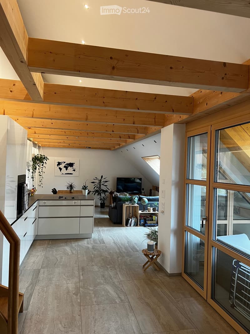 Open-plan living and dining area with exposed wooden beams, modern kitchen, large windows, and a cozy seating area.