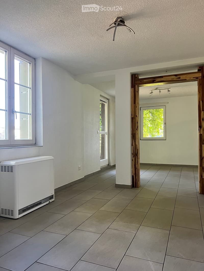 Empty hallway with tiled floor, white walls, large windows, and a radiator on the left side.