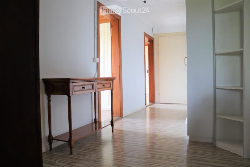 Empty hallway with wooden console table, white walls, wooden floors, doors leading to different rooms