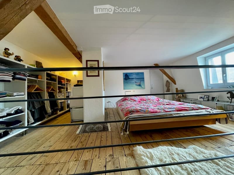bedroom with wooden floor, bed, rug, wardrobe, shelves, window, painting, metal railing