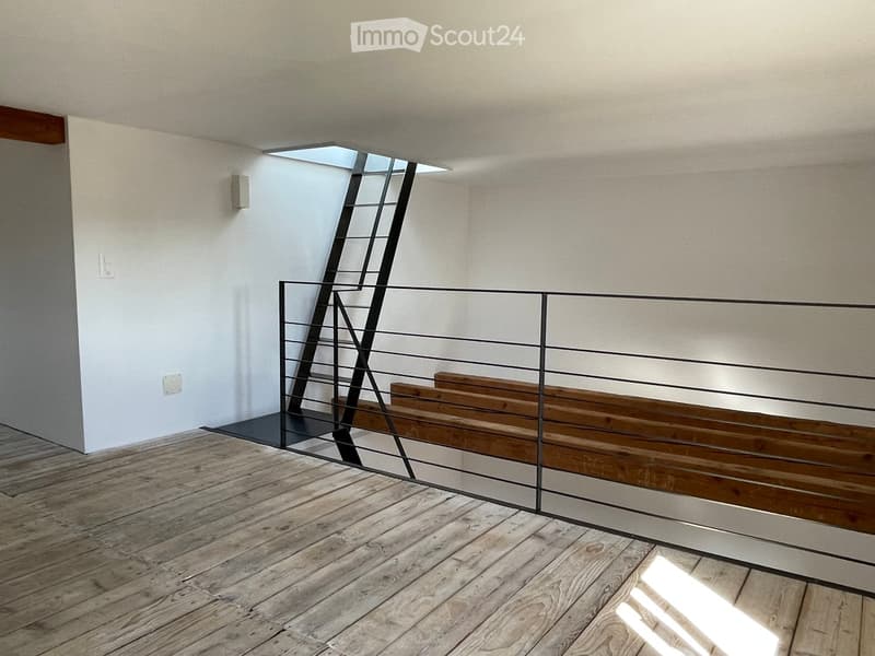 empty room, wooden floor, black railings, wall mounted light, ladder leading to an attic
