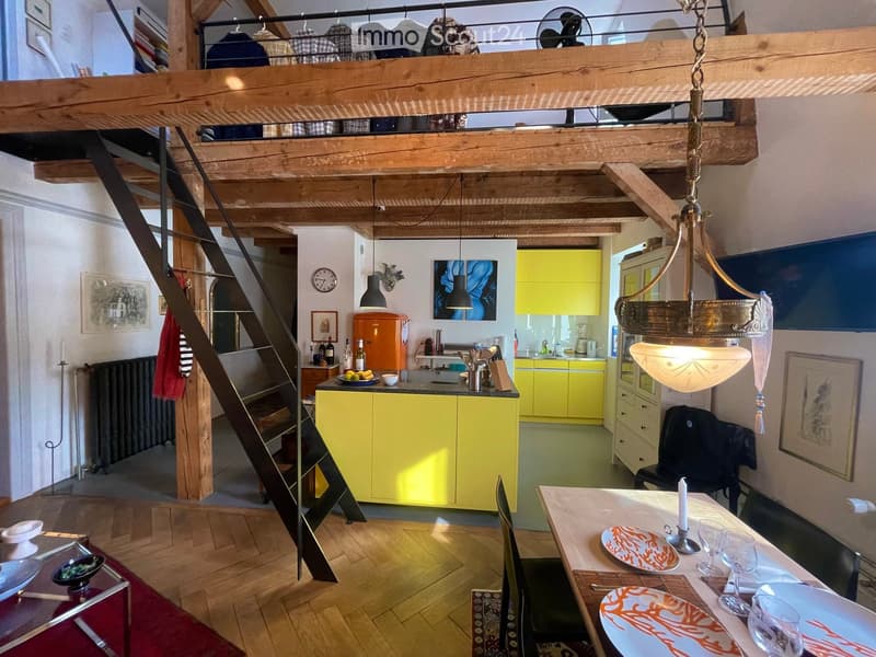 Open concept living room and kitchen, wooden beam ceiling, yellow kitchen cabinets, chandelier, open loft bedroom, stairs leading to loft bedroom, dining table, radiator, artworks on the wall