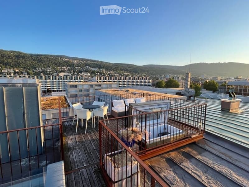 Rooftop terrace with wooden deck, metal railings, white chairs, round table, lounge chairs, potted plants, and a view of the city and mountains