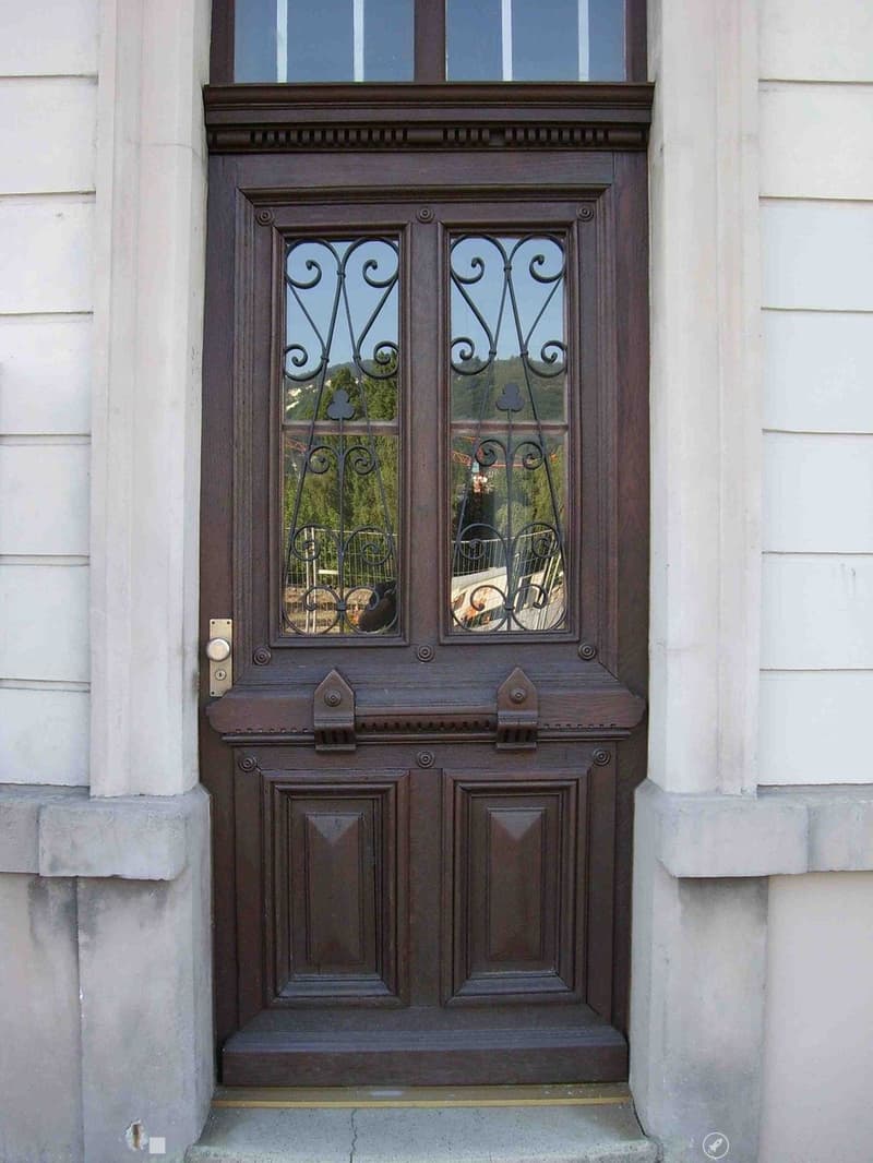 brown wooden door with glass panels, metal grills, white wall, concrete steps