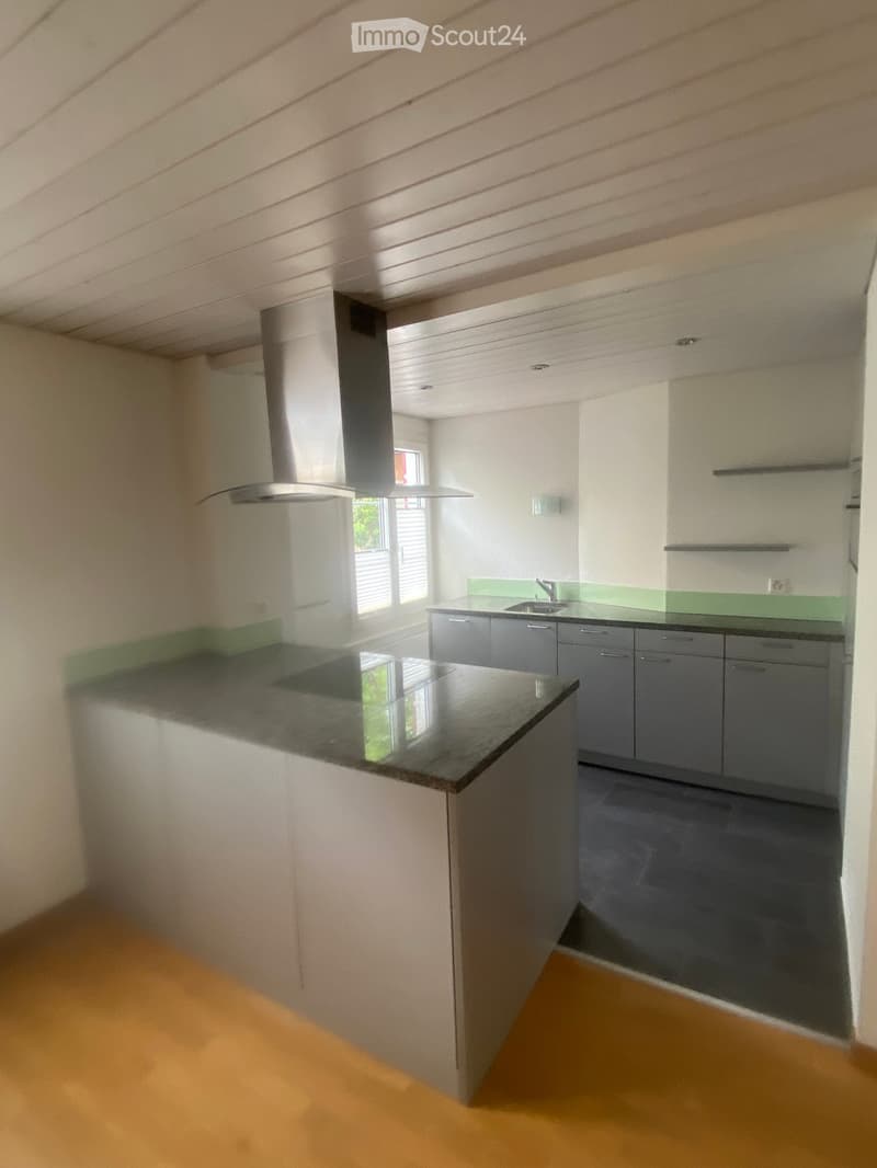 Modern kitchen with grey cabinets, black countertop, and a central island. Features a stainless steel range hood and a window above the sink.