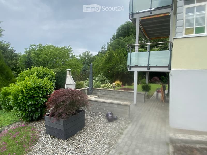 Well-maintained garden with a raised planter, gravel pathway, modern outdoor furniture, and a view of a house with a balcony.