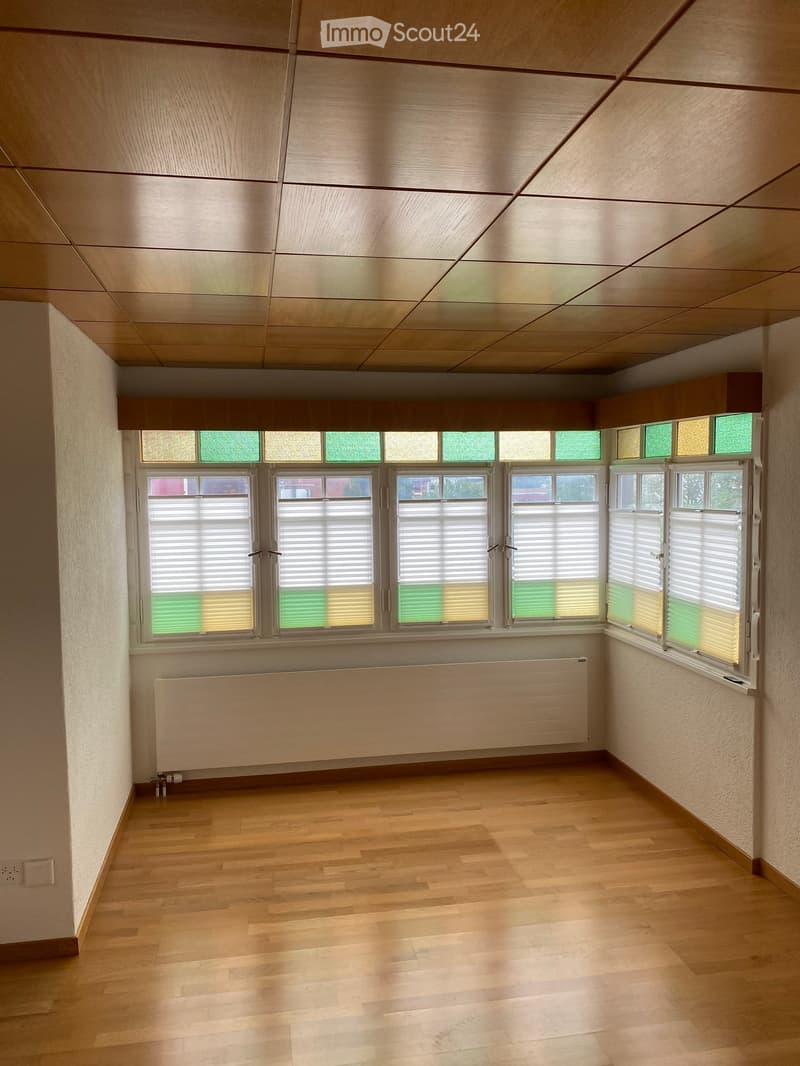 Empty room with wooden flooring, large windows with blinds, and a radiator under the windows.
