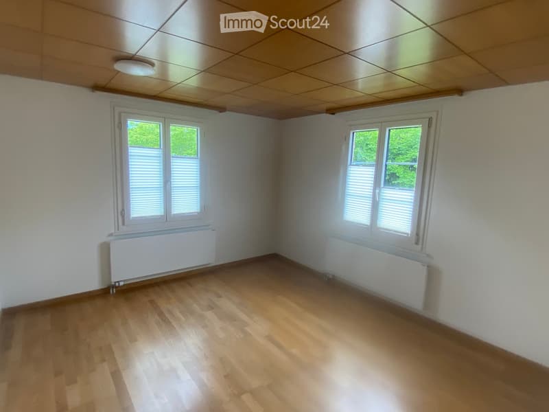 Empty room with wooden flooring, white walls, and two windows with blinds. Radiators are visible beneath the windows.