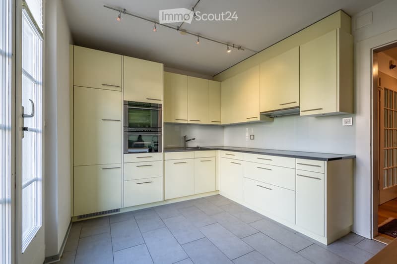 Modern kitchen with light-colored cabinets, stainless steel oven, sink, and faucet. Track lighting above the counter.