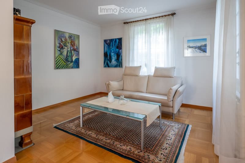 Living room with a white leather sofa, glass coffee table, wooden floor, and artwork on the walls.