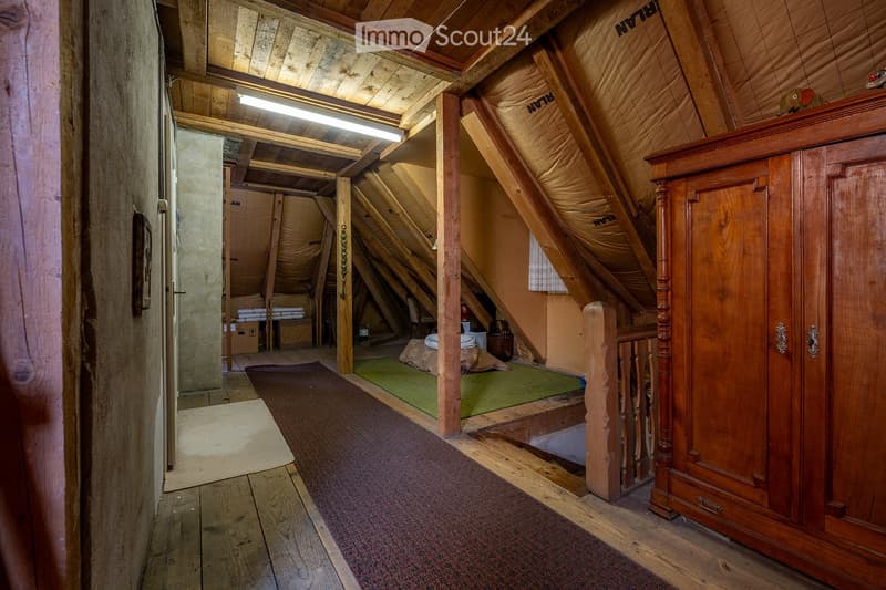 Attic room with wooden beams, exposed wooden floor, a large wardrobe, a small bed, a chair, and a table.