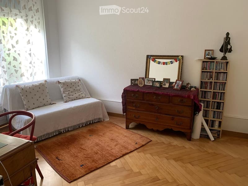 Cozy living room with a sofa, wooden bookcase, mirror, and small table with framed photos.