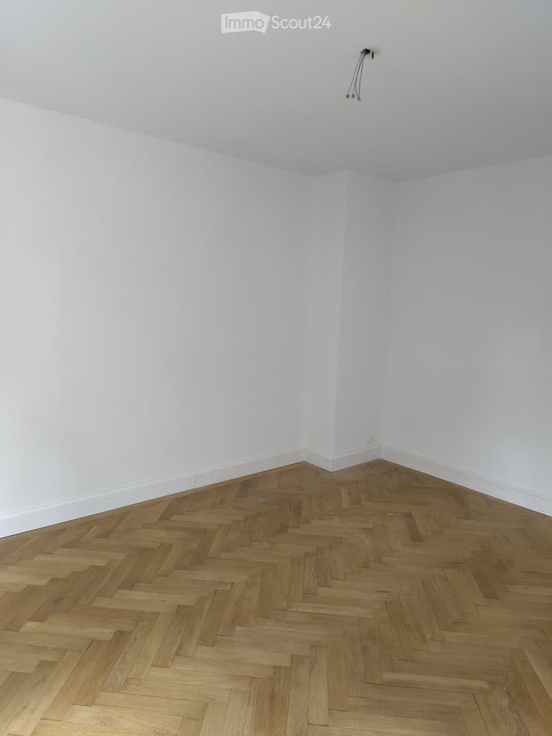 Empty room with white walls and herringbone wooden flooring. No furniture or equipment present.