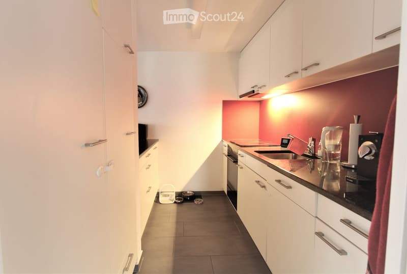 Modern kitchen with white cabinets, stainless steel appliances, and a red accent wall. Includes a sink, coffee maker, and various kitchen items on the counter.