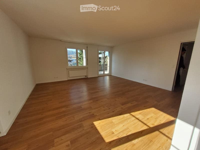 Empty room with wooden flooring, white walls, large windows, and a sliding glass door leading outside.