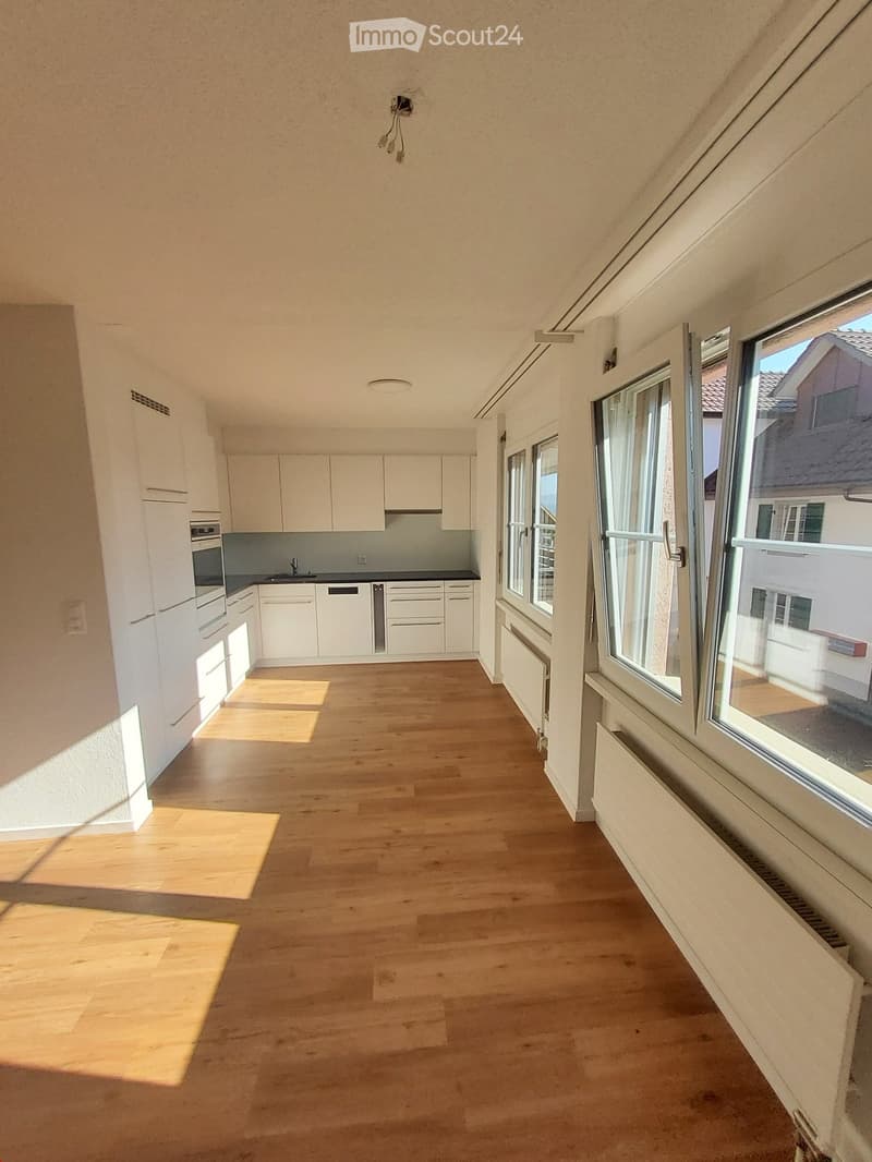 Empty room with wooden flooring, white cabinets, and large windows allowing natural light to enter.