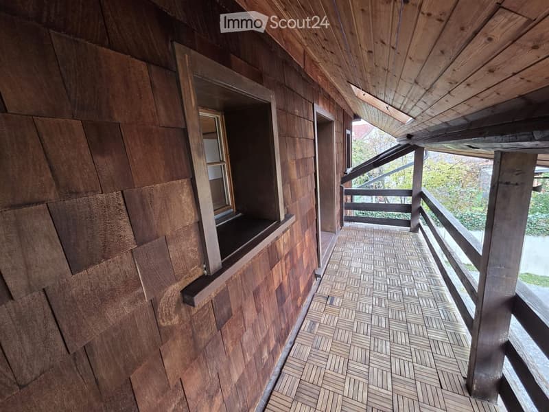 Balcony with wooden railings, wooden wall siding, window with sill, tiled floor