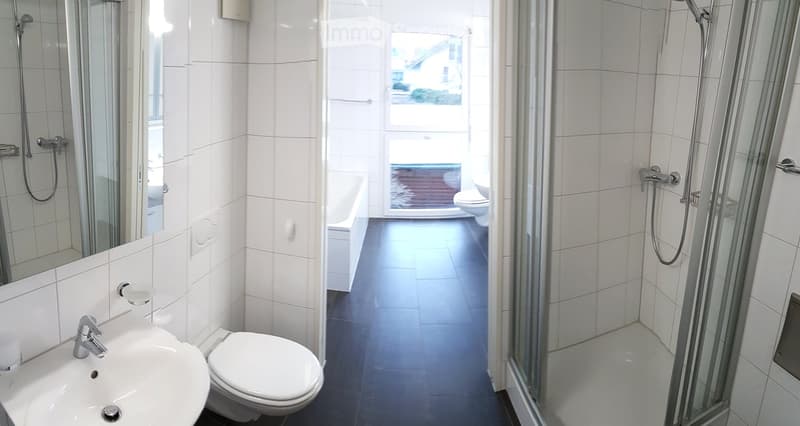 Bathroom. Modern bathroom with white tiles, a sink, toilet, and a shower area.
