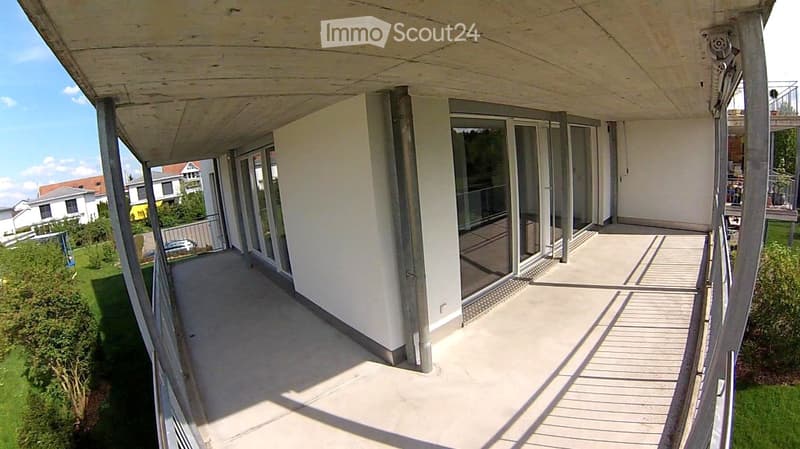 Balcony / Terrace. An empty balcony with a concrete floor and glass railings, overlooking a grassy area with bushes and a parked car.