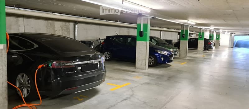 Corridor / Hallway. Underground parking lot with cars parked and charging stations. A bicycle is also parked.