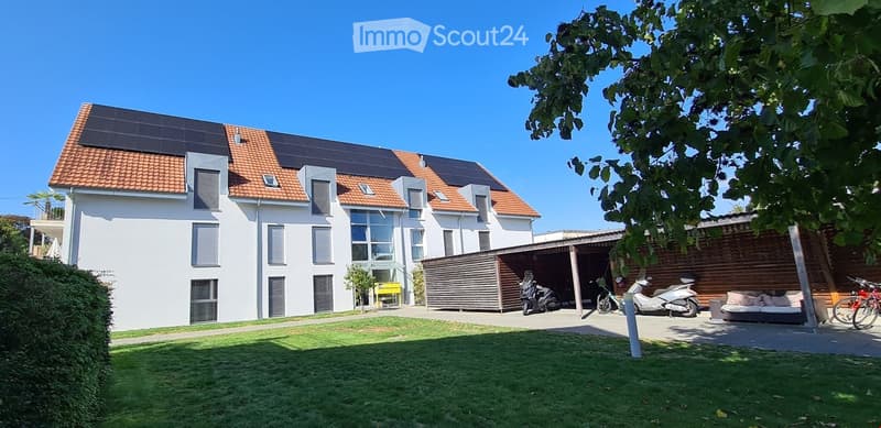 House. Modern white house with solar panels on the roof, bicycles and motorcycles parked in front, and a couch under a tree.