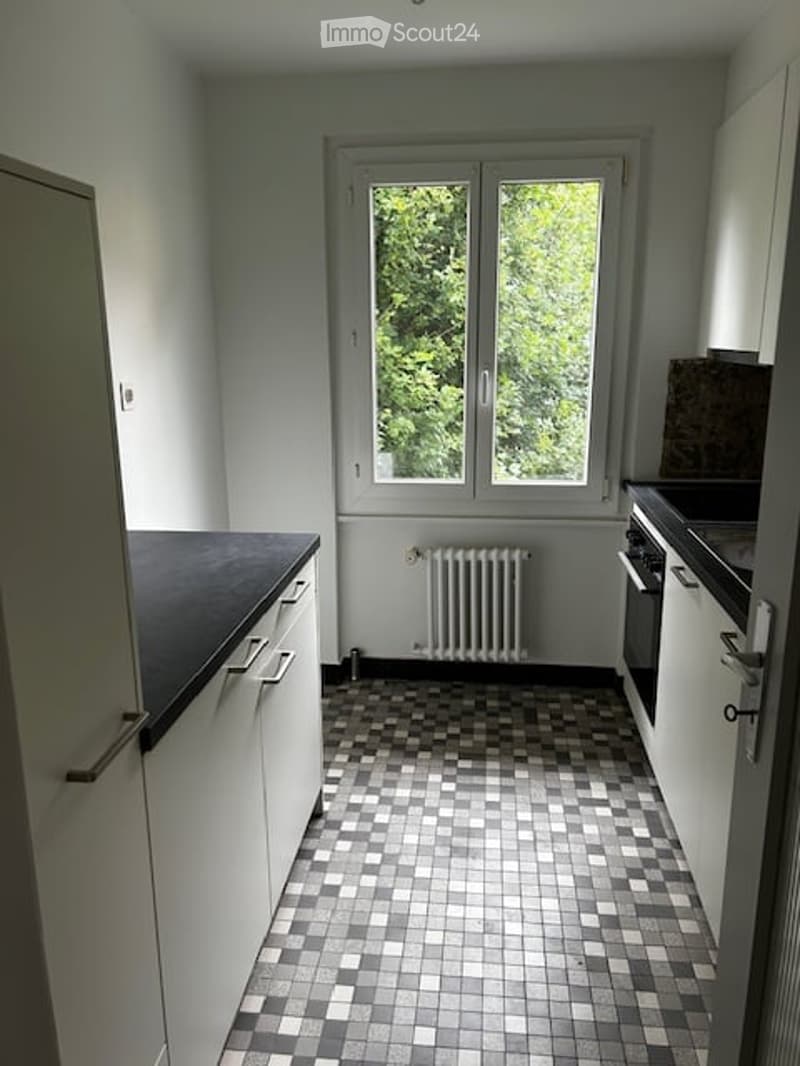 Modern kitchen with white cabinets, black countertop, checkered tile floor, and a window overlooking greenery.