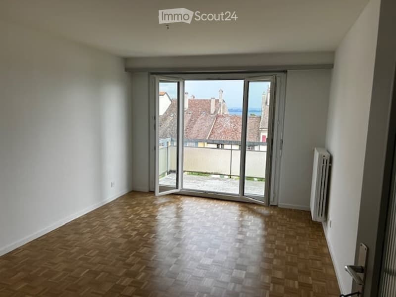 Empty room with wooden flooring, large sliding glass doors leading to a view of rooftops and water.
