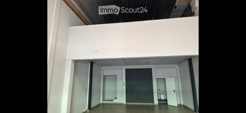 Open, modern corridor with white walls, a raised platform above, and a small bathroom area visible to the right.
