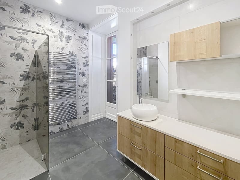 Modern bathroom with a glass-enclosed shower, a white sink with a modern faucet, a large mirror, and wooden cabinets.
