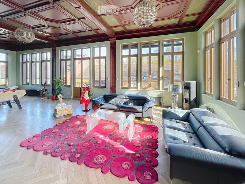 Spacious living room with wooden floors, large windows, two sofas, coffee table, decorative rug, table lamps, and a chandelier.