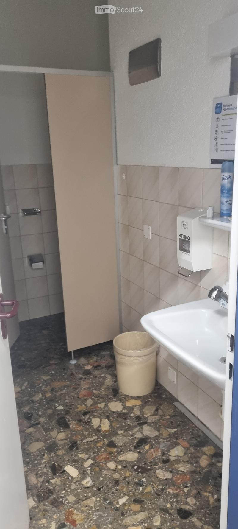 Bathroom with a sink, faucet, hand dryer, and a trash can on a stone-tiled floor.