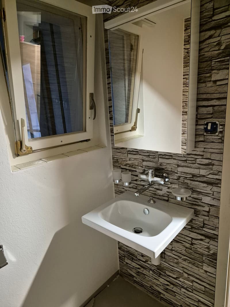 Modern bathroom with a stone-textured wall, white sink, chrome faucet, and built-in mirror cabinet.
