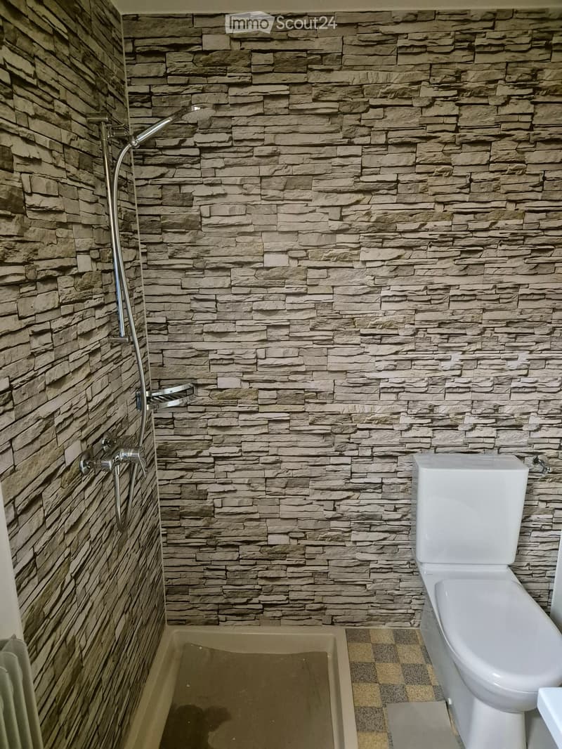 Modern bathroom with stone-textured walls, a bathtub, a toilet, and a showerhead with a handheld sprayer.