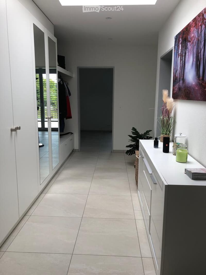 Modern hallway with tiled floor, white walls, built-in closet with mirrored doors, and a small console table with decorative items.