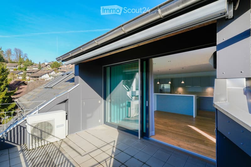 Modern balcony with tiled flooring, large glass sliding doors leading to an interior space, visible air conditioning unit, and a view of a residential neighborhood with trees and houses.